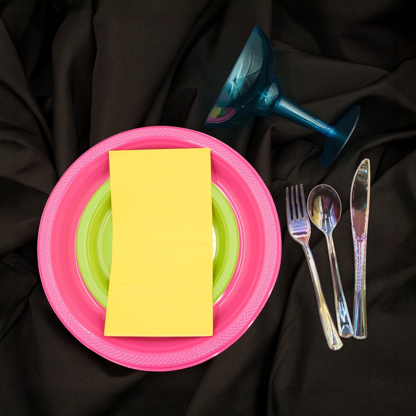 Pink plate with a yellow napkin, green plate, cutlery, and margarita glass, black tablecloth