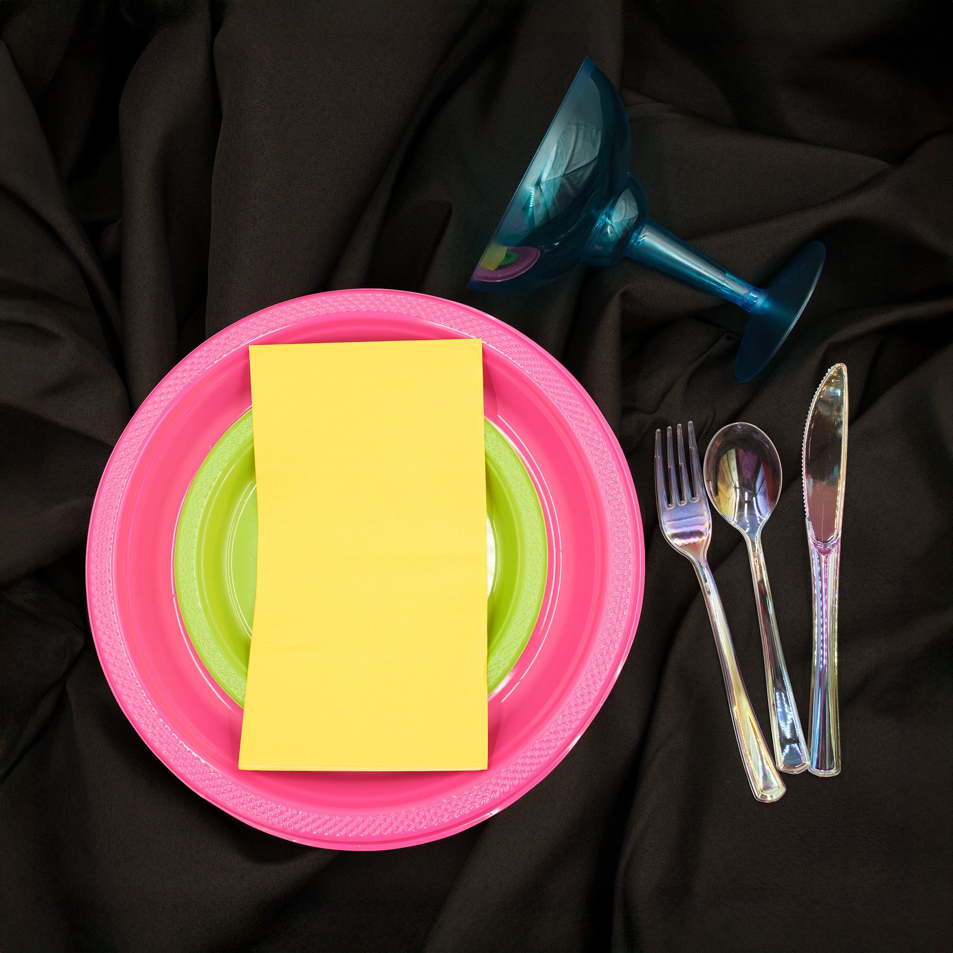Pink plate with a yellow napkin, green plate, cutlery, and margarita glass, black tablecloth