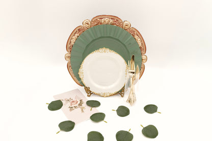 Decorative place setting with gold charger, sage green and ivory plates, gold silverware, and eucalyptus leaves table scatter